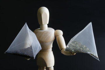 An anthropomorphic mannequin holds pyramid tea bags with black and green tea. Concept for consumer...