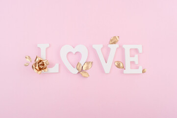 Word Love with gold rose and leaves one the pink background. Creative composition. Valentines day.