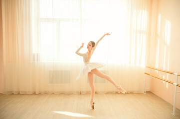 Fototapeta premium Beautiful ballerina in body and white tutu is training in a dance class. Young flexible dancer posing in pointe shoes.