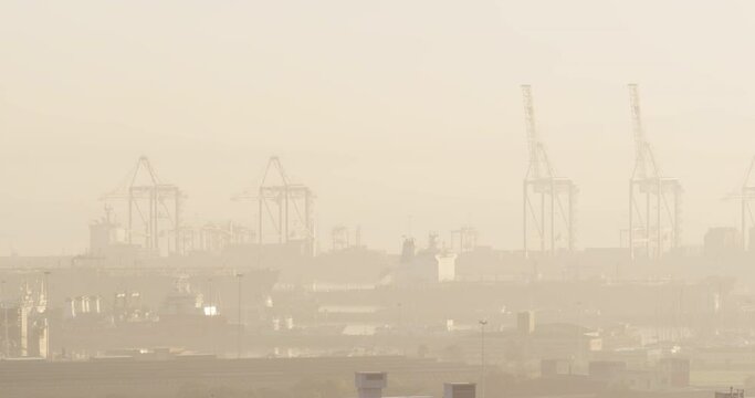 General view of cityscape with multiple buildings and shipyard covered in fog
