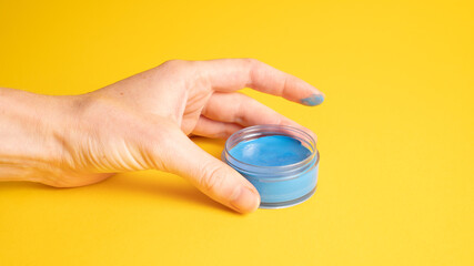 Blue skin paint in a container. Blue foundation in blue hand on yellow. Theatrical makeup base