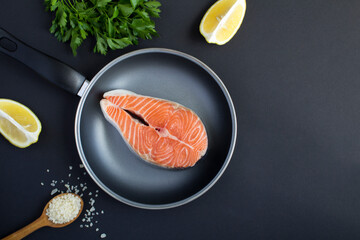 Top view of raw fish salmon in a frying pan on the black background. Close-up.Copy space.