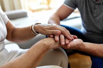 Man holding senior woman's hand at home. Male healthcare worker holding hands of senior woman at care home, focus on hands. Shot of a young man hands holding old senior elderly hand with love and care