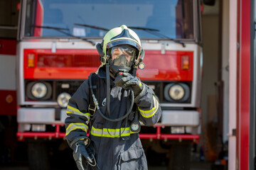 Child, cute boy, dressed in fire fighers cloths in a fire station with fire truck