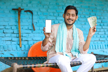 Indian farmer showing smartphone and money at home.