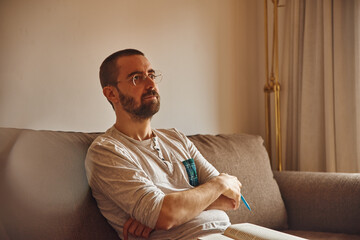 Reflective man sitting on couch with folded arms