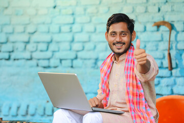 Indian farmer using laptop and showing thumps up at home. - obrazy, fototapety, plakaty