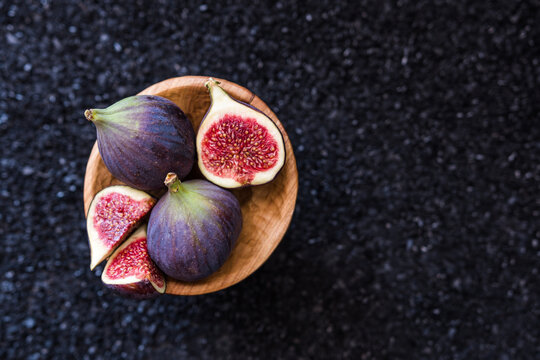 Top view of fig fruits in a small wooden bowl on black background.