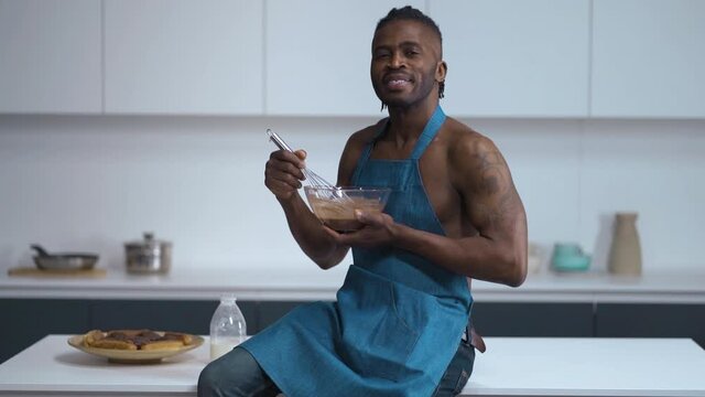 Sexy man. Handsome African on kitchen in blue cover-slut. Cook lick a Choco cream from wire whisk. High quality FullHD footage.