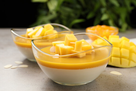 Delicious panna cotta with mango coulis and fresh fruit pieces on grey table