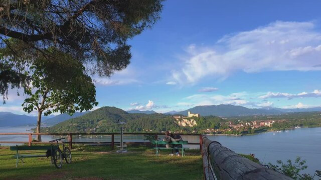 Back View of Romantic Man and Woman Sitting Together and Looking at Beautiful Landscape of Maggiore Lake. Italy