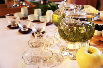 Chinese style tea accessories, transparent cups on transparent and brown coasters, on the right, two transparent teapots with tea and an apple