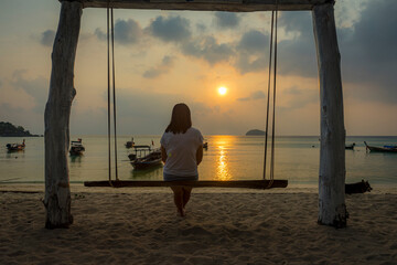 A woman sitting on a swing watching the sunrise alone
