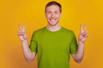 Photo of attractive positive cool guy raise hands make v-signs peace cool funky isolated on yellow color background