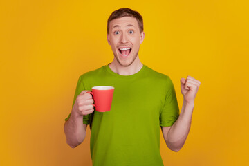 Photo of young man happy positive smile drink coffee cup rejoice victory success isolated over yellow color background