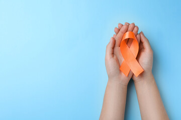 Woman holding orange ribbon on light blue background, top view with space for text. Multiple...