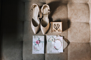 Wedding accessories for the bride close-up: a wooden box, gold rings, women's beige shoes, a garter, a decorated envelope, an invitation.