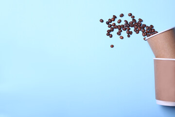 Scattered coffee beans from a paper cup on a blue background.