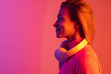 Side view portrait of young beautiful smiling girl isolated over gradient background in neon lights.