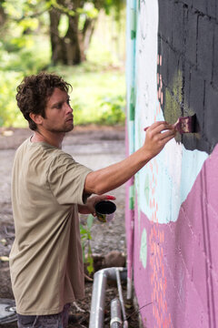 Concentrated Male Artist Painting Mural On Wall