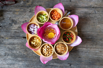 Miang kham is a traditional snack from Thailand. The food wrapped in purple lotus leaves bite-size savour appetizer in dish and bowl. and side dish such as chili, lemon, nut. It on the wooden table 