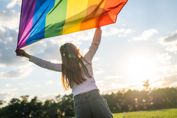 Symbol of love, freedom or LGBT pride concept. Girl holding the rainbow flag against the blue sky background, outdoors in the summer. Liberty right, proud to be equal and legal marriage.