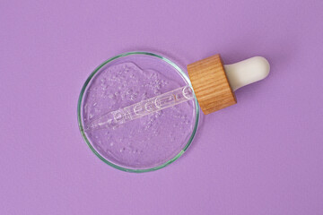 Pipette from dropper with wooden cover lies in the petri dish with cosmetics gel.Top view,liquid cosmetic,macro photography.Lilac banner with copy space.