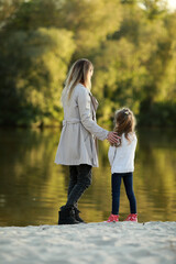 Mother and daughter walk on beach near river.