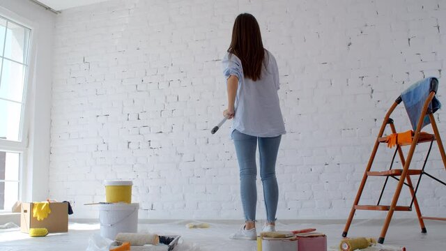Young caucasian woman decorating wall doing house renovation. A female painter painting wall with roller redecorating apartment. Home improvement concept. New home concept. 4k slow motion