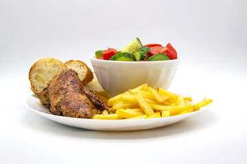 Fried chicken breast with fries, slices of bread and salad in a white plate on a light background. Fresh salad with cucumbers and tomatoes. Very tasty lunch.