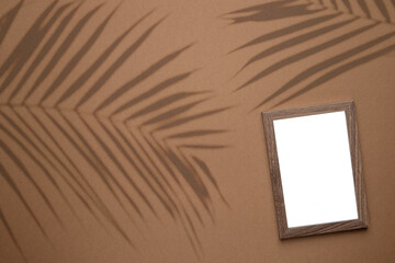 Blank picture frame on trend brown background with tropical plant shadow light as template for event promotion, design presentation, self portfolio etc.