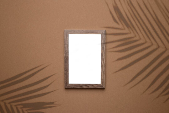 Blank picture frame on trend brown background with tropical plant shadow light as template for event promotion, design presentation, self portfolio etc.