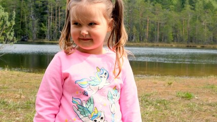 Portrait of a laughing 3 year old girl, dressed in a pink sweatshirt with two ponytails, playing outdoors in nature. Happy childhood concept, children development