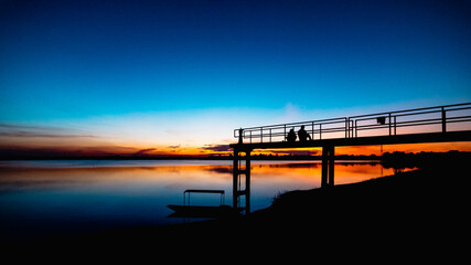 Fototapeta premium Two silhouette people on the bridge with a sunset background and a boat