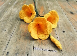 Crochet Allamanda flowers on the wooden background in handmade concept and selective focus