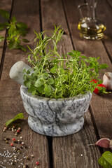Fragrant herbs in mortar on wooden table with condiments and oil