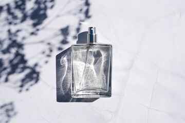 Transparent bottle of perfume with spray on white marble surface. Clear glass without lid. Trending...