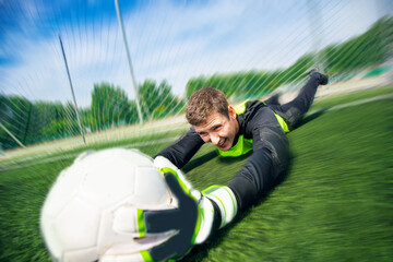 Naklejka premium Goalkeeper soccer man catching ball in stadium, action moment of sport