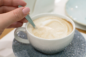 Girl mixes sugar with a spoon in a beautiful cup of fresh coffee. Breakfast at the cafe.