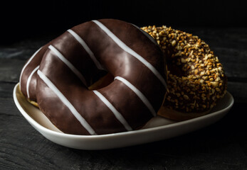 Delicious glazed doughnuts on a white plate and black background.