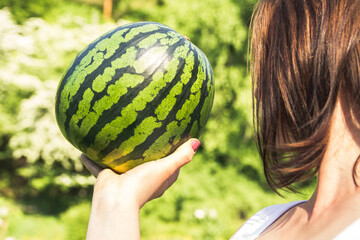 Young girl holding whole watermelon on a sunny summer day.