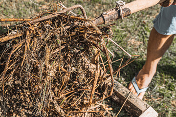 man farmer sorts out compost with pitchfork in compost bin in backyard of country house