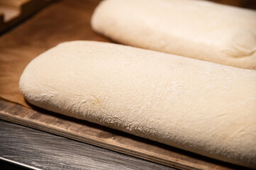 A piece of raw French bun dough against the background of other bun dough pieces. Raw craft bread dough
