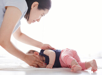 Naklejka premium Cute Asian mom helps baby turn overCute Asian mom helps baby stand up exercises