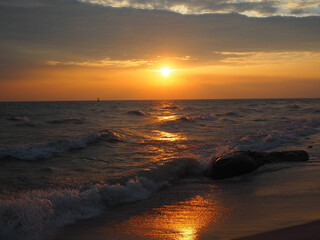 Beautiful sky over the sea at sunrise, orange bright light, waves lapping on the beach.