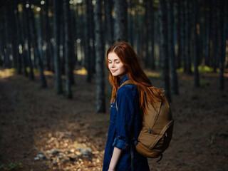 cheerful red-haired woman with a backpack in the woods travel