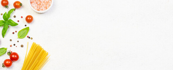 Raw spaghetti, Himalaya salt, cherry tomatoes and fresh aromatic basil on white marble background with copy space for your design. Food blog template. Recipe book cover mock up. Long banner format.