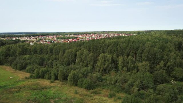 Panoramic footage. Flying over the forest, a view of a modern suburban village opens up. 