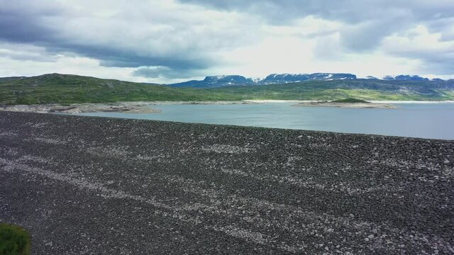 Approaching water reservoir dam for hydroelectric powerplant - Sysendammen Norway - spectacular view over gigantic dam and dramatic clouds - Hardangervidda national park aerial