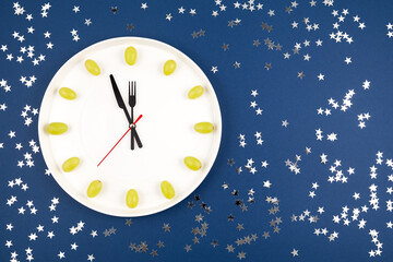 Clock made of grapes on blue background with sequins. Latin American and Spanish New Year tradition...